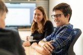 Smiling intern with the glasses talking to colleagues in the office.Positive atmosphere in the office with young interns and with a supervisor_ Smiling boy talks to employees