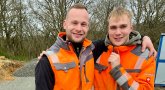 Two male Stadtwerke employees laugh into the camera on the construction site