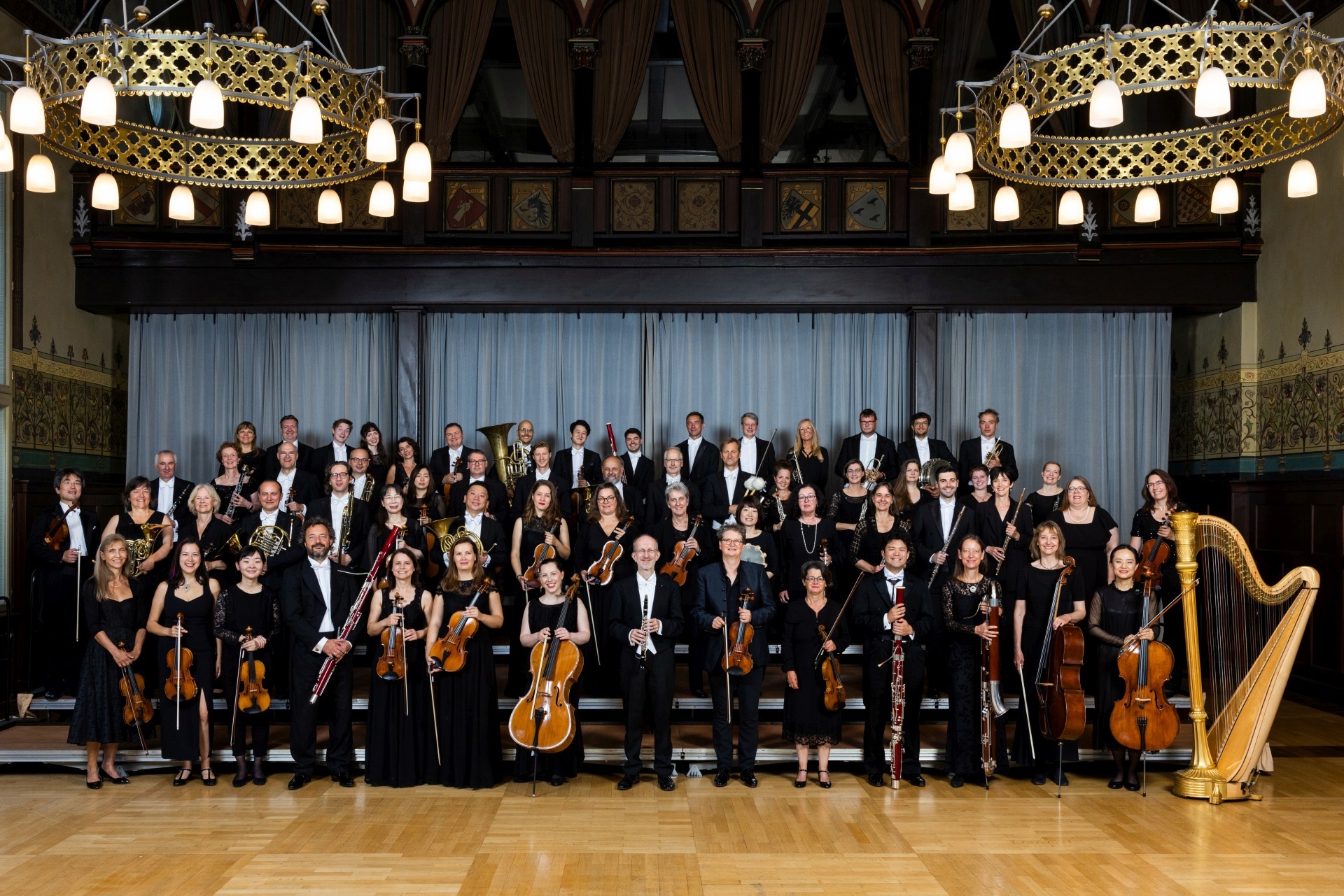 The photo shows the orchestra members in four ascending rows in a ballroom.
