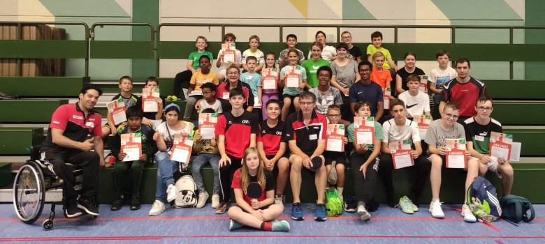 The photo shows a group picture of the participants sitting on the steps of the grandstand in the Stadenhalle.