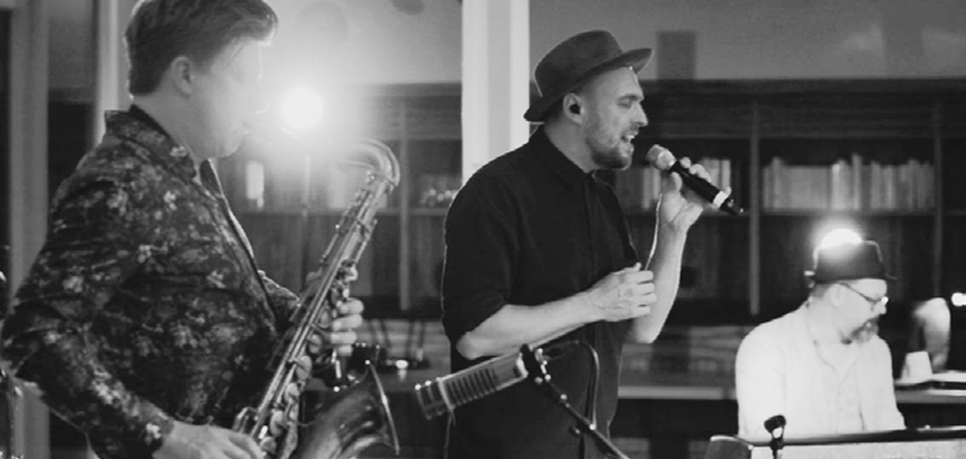 The black and white photo shows a saxophonist in the foreground, Max Mutzke singing with a microphone behind him and Matti Klein on the keyboard in the background.
