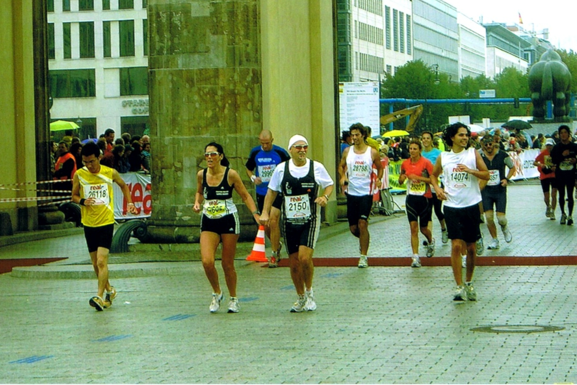 The photo shows several runners crossing the finish line of the Berlin Marathon at the Brandenburg Gate. Ilonka and Rainer Hagner can be seen in the center of the picture, crossing the finish line hand in hand.
