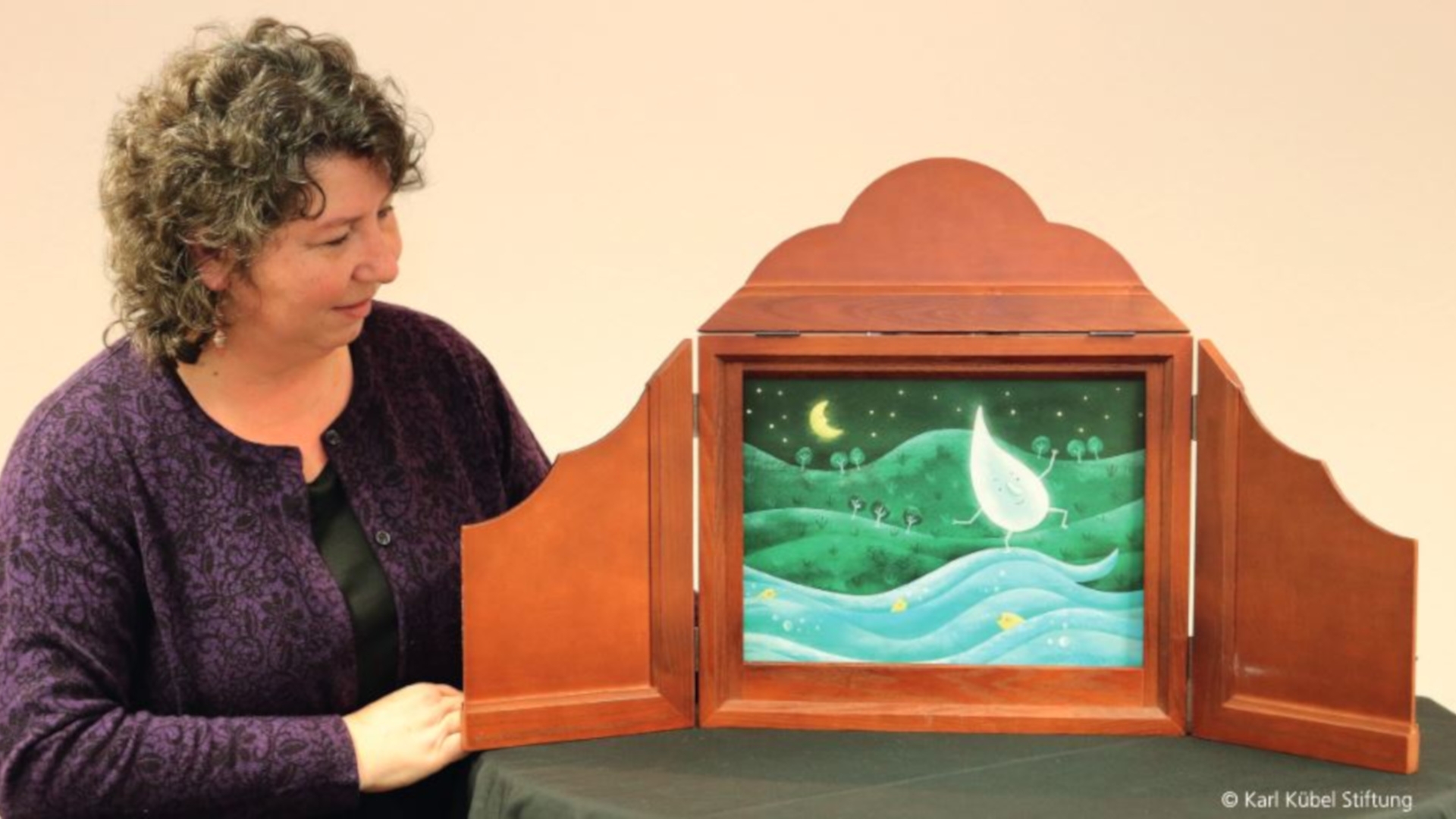 The photo shows a woman standing next to a Kamishibai frame.