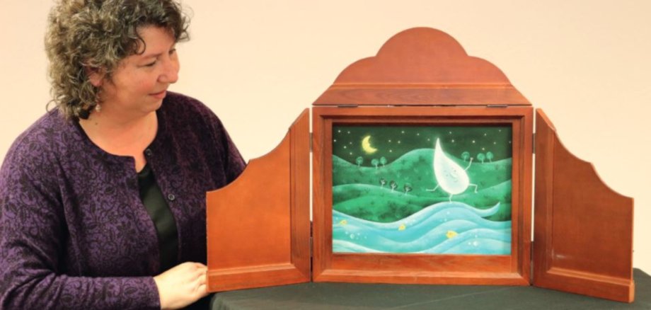 The photo shows a woman standing next to a Kamishibai frame.
