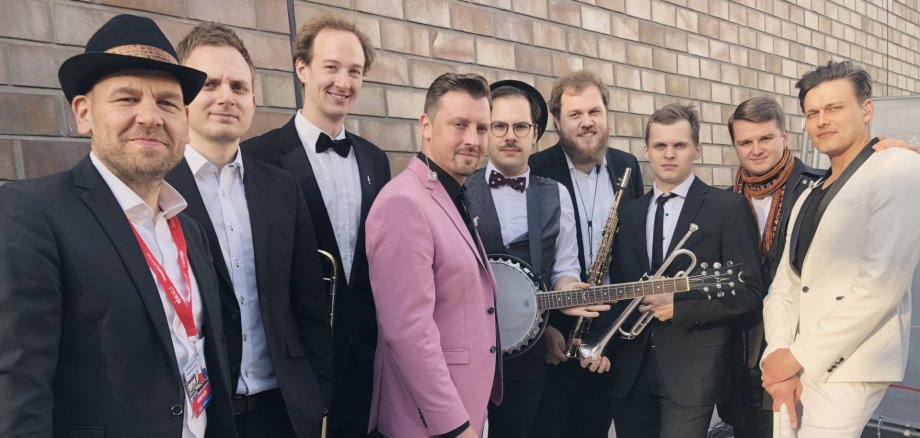 The photo shows the musicians in front of a stone wall.