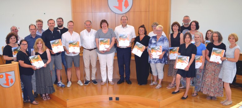The photo shows all participants in the ceremony standing in front of the boardroom bench with their folders.