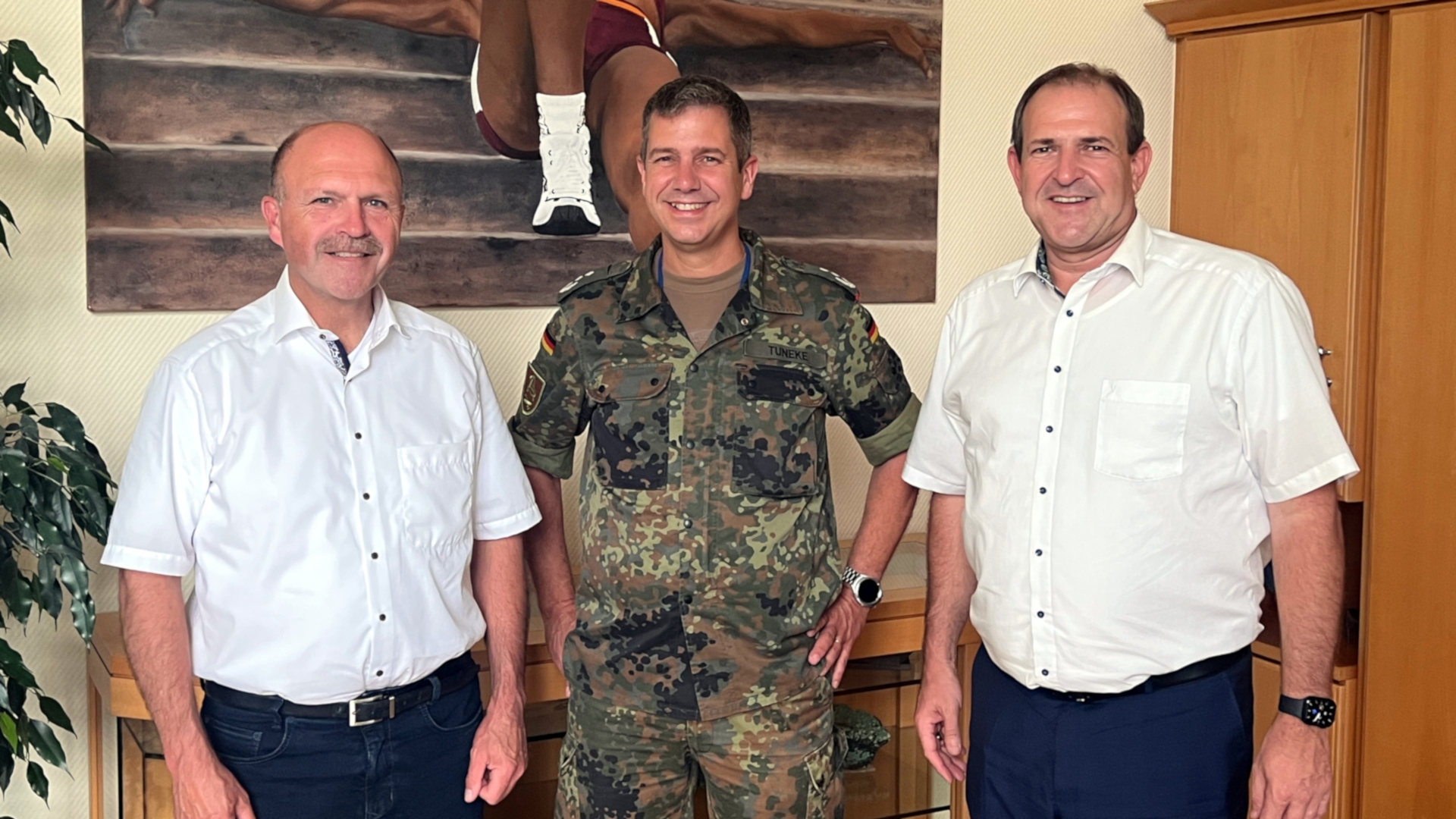 The photo shows, from right to left, Mayor Frank Frühauf, Colonel Olaf Tuneke and Mayor Friedrich Marx standing in front of a wall with a painting in Mayor Frühauf's office and looking into the camera.