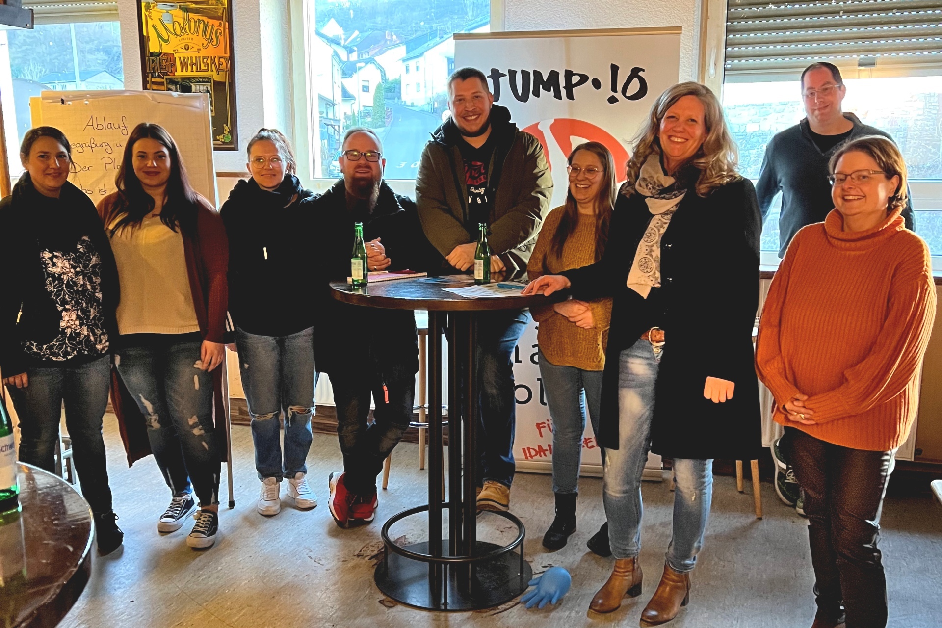 The photo shows nine participants of the meeting at a bar table.