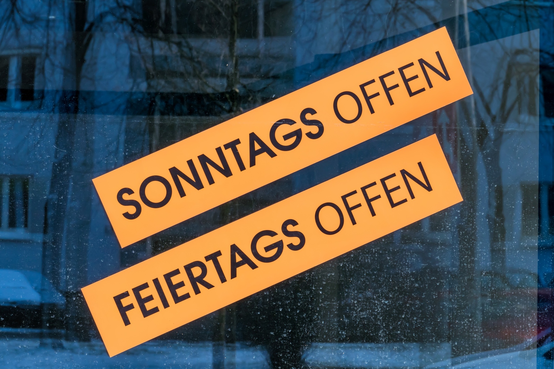 The photo shows a shop window with the two stickers "Open on Sunday" and "Open on public holidays".