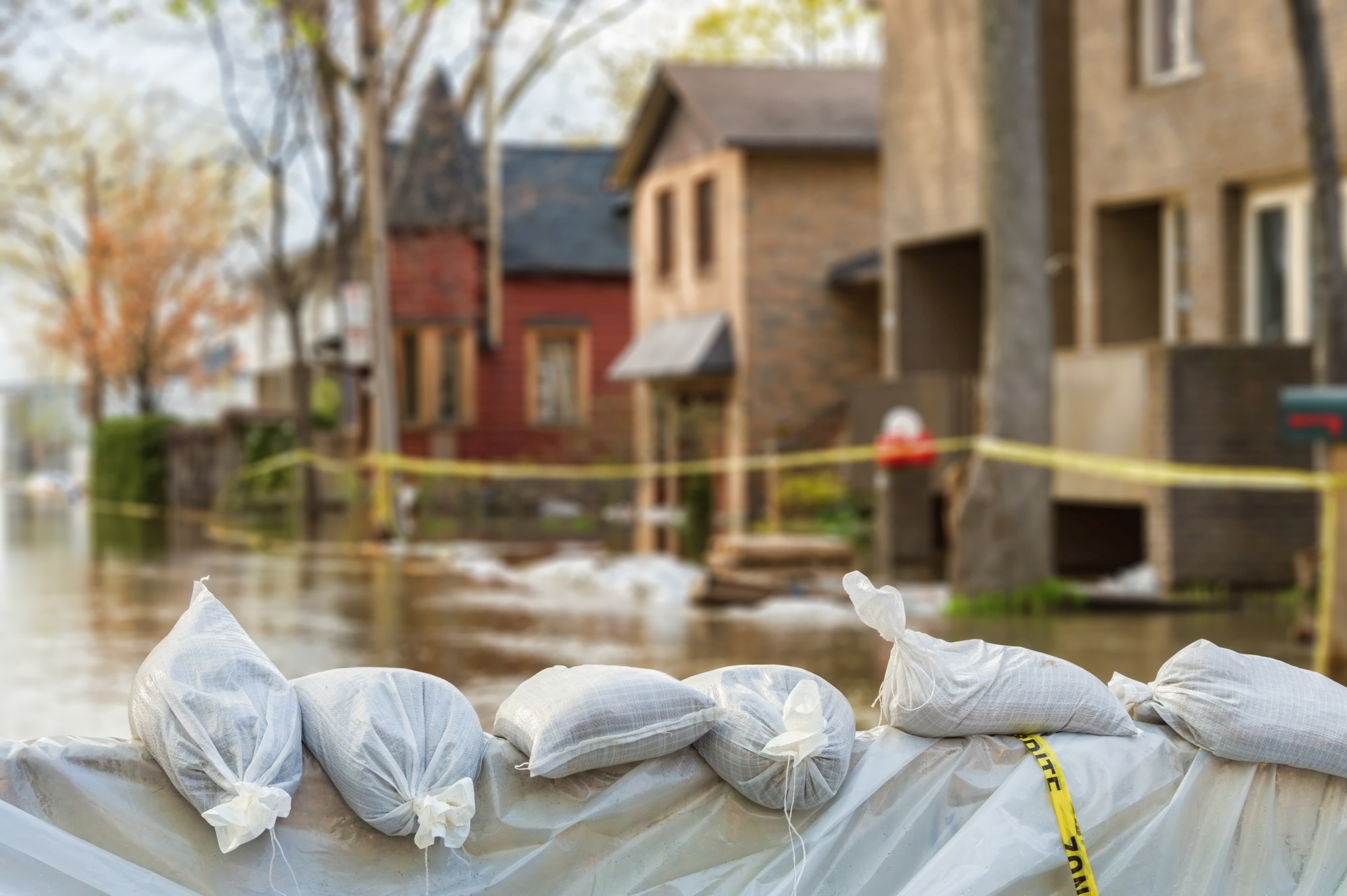 The photo shows a row of sandbags in front of a flooded house front.