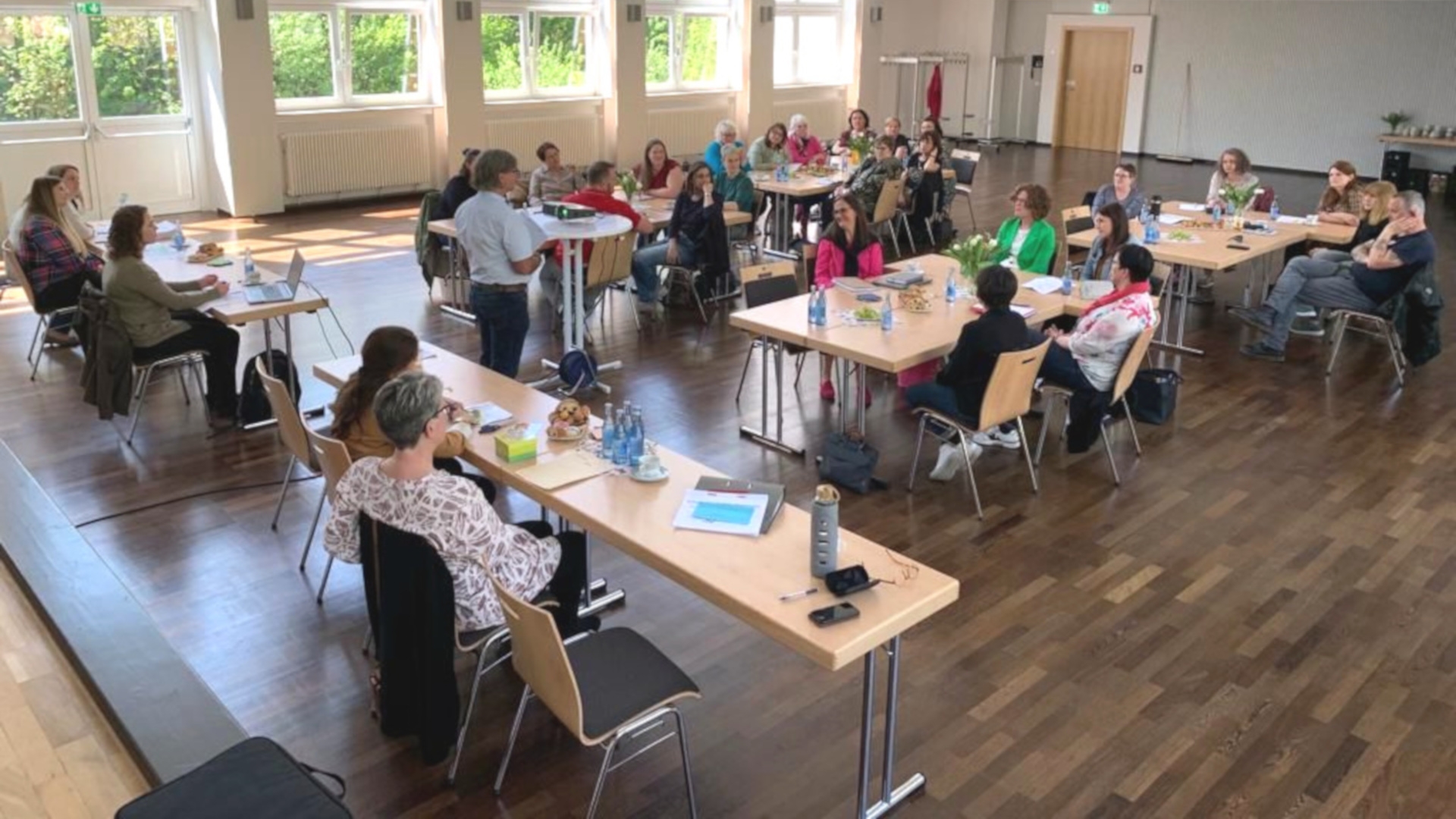The photo shows the participants of the management conference sitting at tables in the Göttenbach auditorium. Heinz Müller stands in their midst and gives a talk.