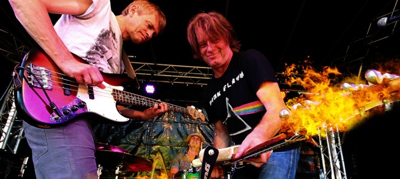The photo shows guitarists Thomas Blug and Rudi Spiller on stage, flames shooting out of their guitars.