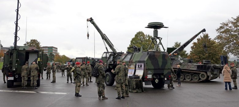 The photo shows some military vehicles, with people standing in front of them and having something explained to them.