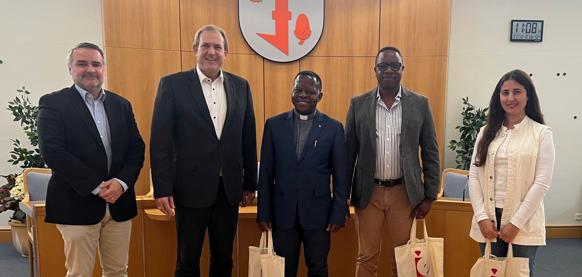 The photo shows the Lord Mayor and four visitors. They are standing on the podium in front of the city coat of arms in the conference room.