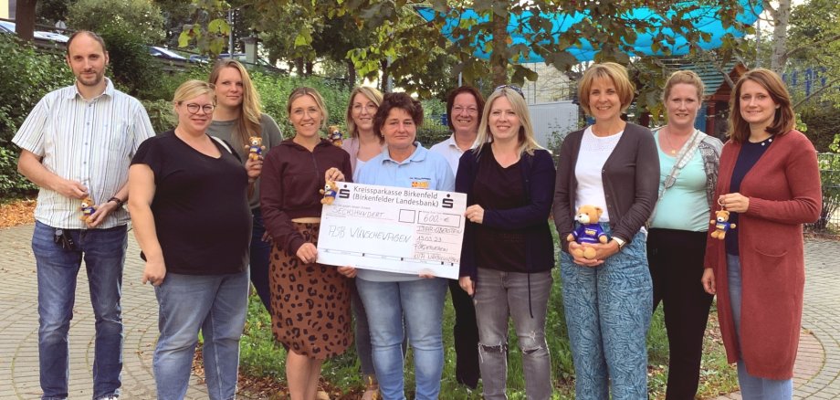 The photo shows nine people standing next to each other in a row. Three women in the middle are holding a large donation check for 600 euros.