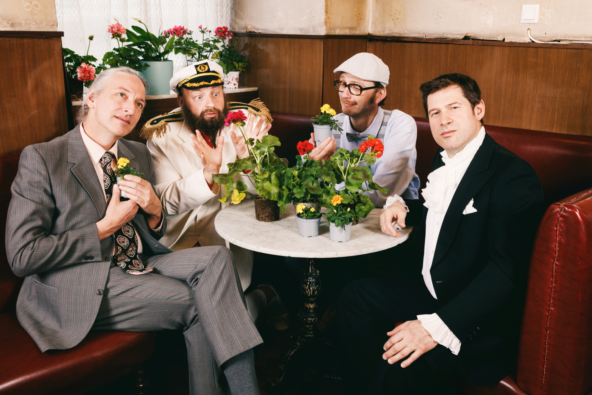 The photo shows the four musicians sitting around a round table in costume.