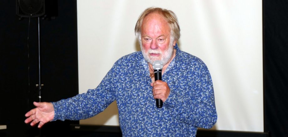 The photo shows the author standing in front of a screen with a microphone during his lecture.