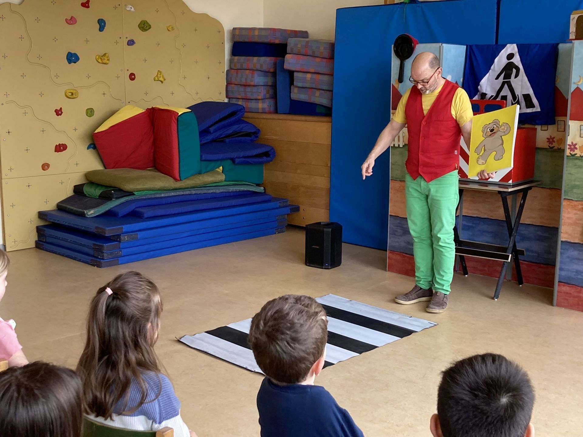 The picture shows the wizard Robert standing in front of a stylized crosswalk and explaining to the children at the daycare center what to do.