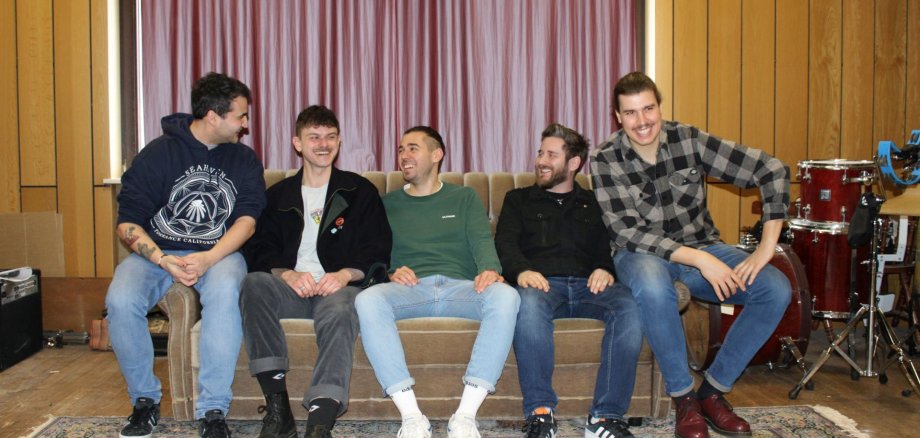 The picture shows the five members of the band summer returns, who are the headliners of the punk rock concert, sitting on a couch.