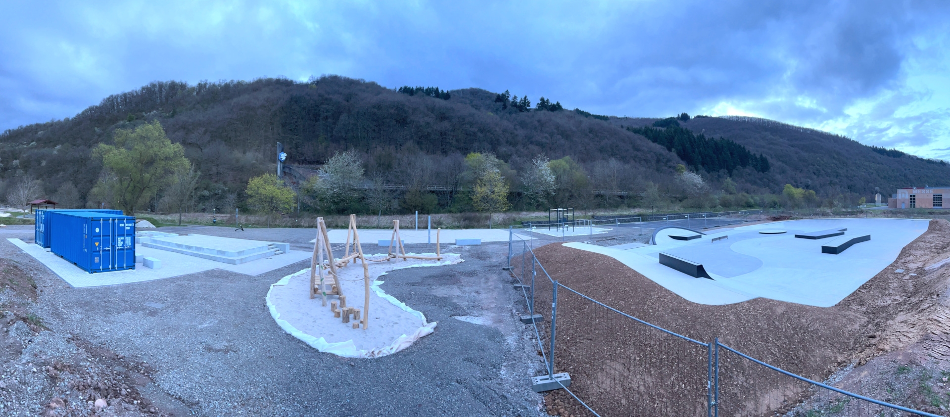 The photo shows a panoramic view of the facility with, from the left, toilet and recreation containers, stage, inclusion swing, beach volleyball court, multi-purpose playing field and skating facility.