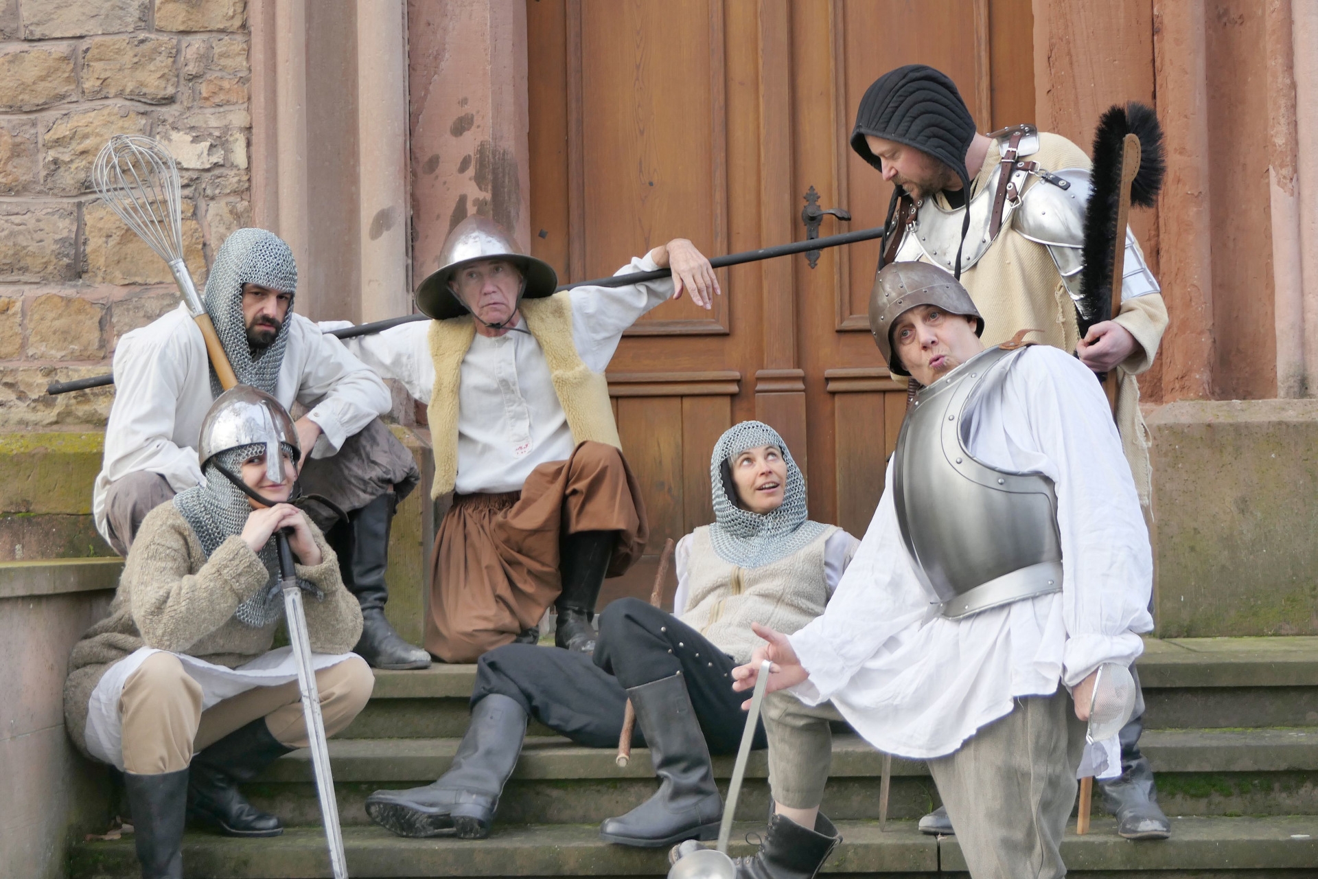 The photo shows actors in knight costumes in front of a stone wall.
