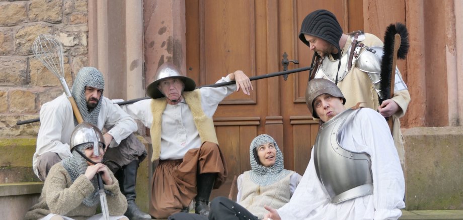 The photo shows actors in knight costumes in front of a stone wall.