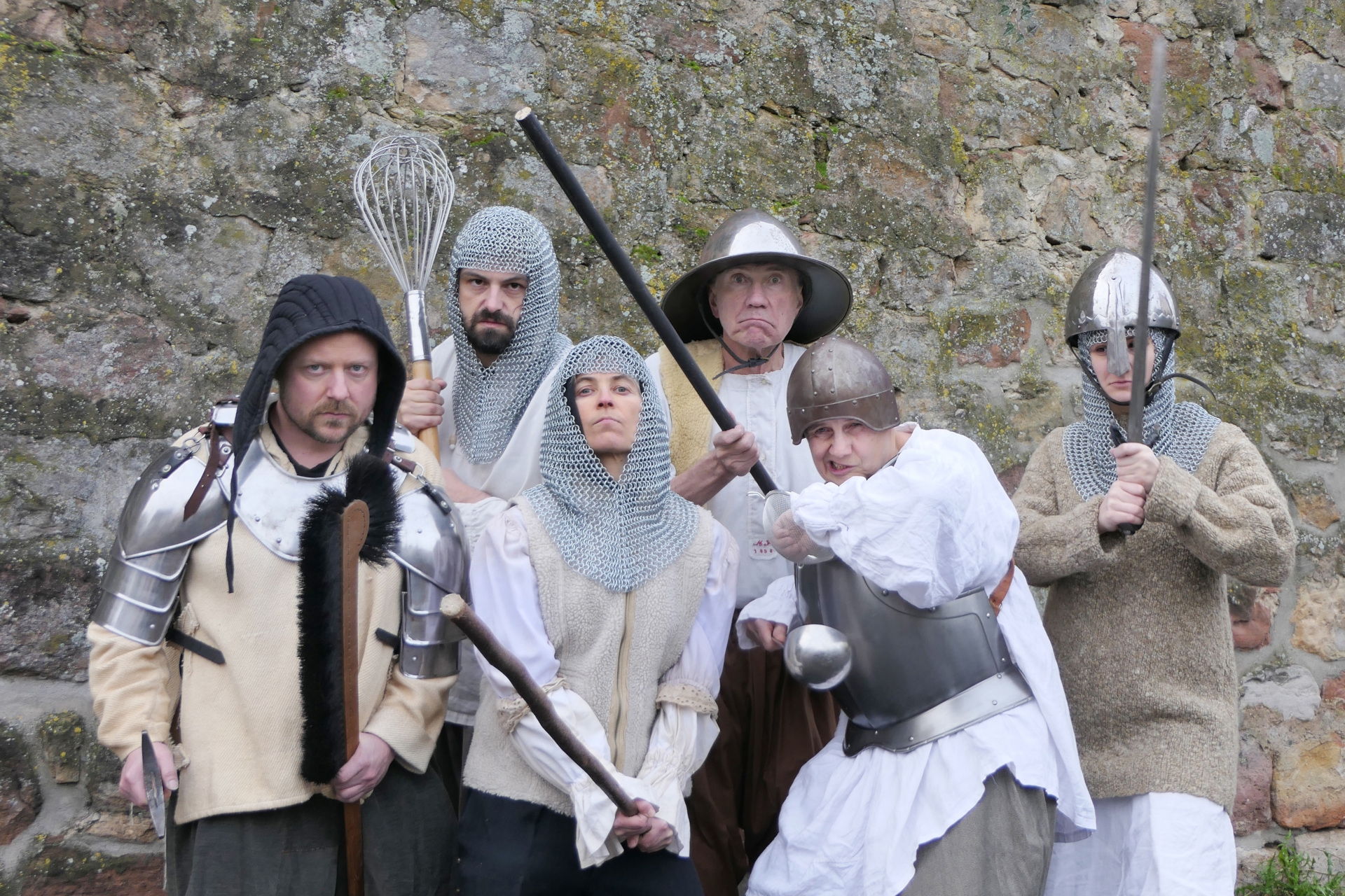 The photo shows the actors in knight costumes with weapons in front of a stone wall.