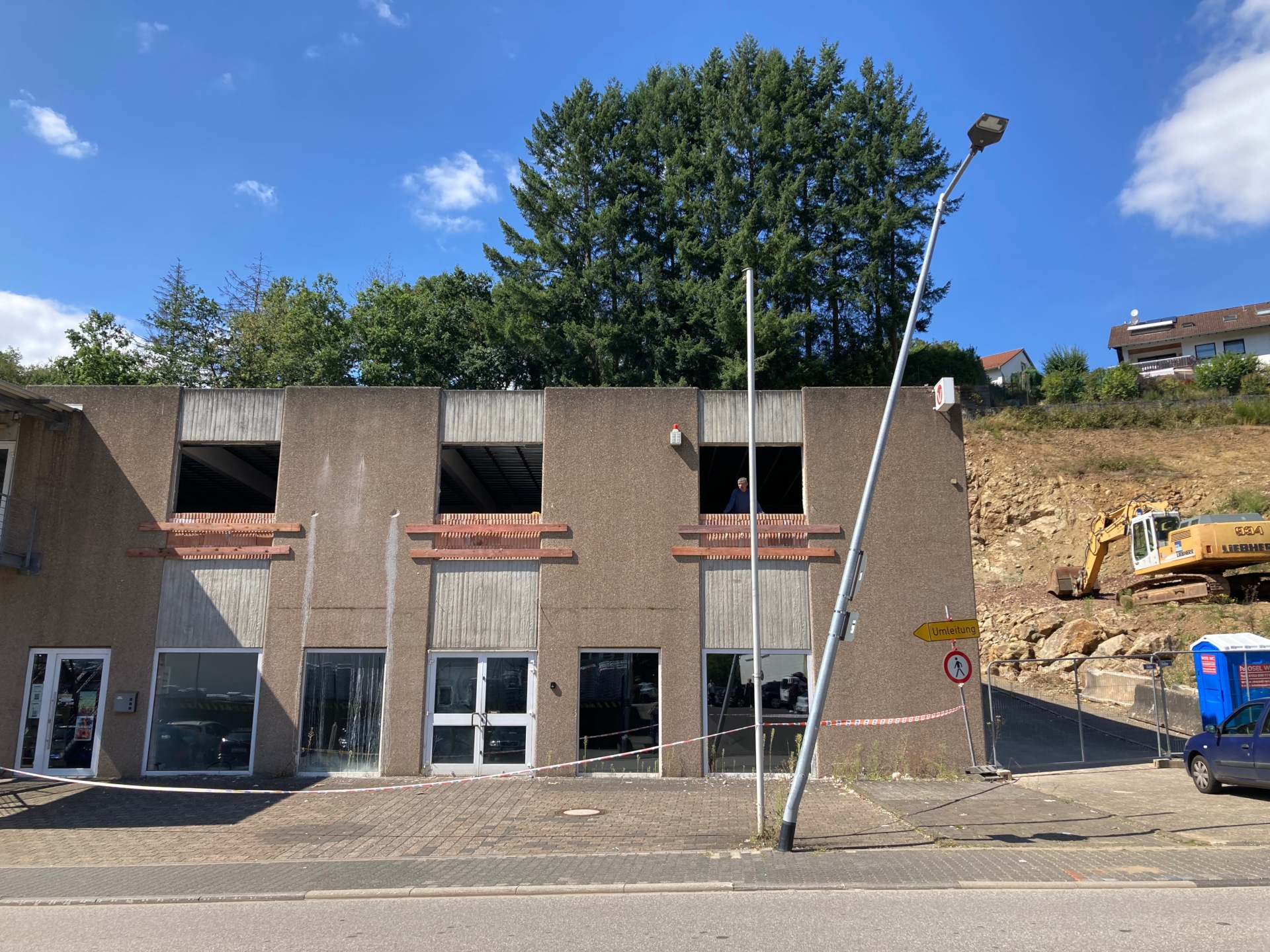 The photo shows the lamppost standing in front of a building. It is leaning due to the accident.