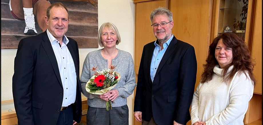 The photo shows the people mentioned. They are standing next to each other in the Lord Mayor's office. The jubilarian is holding a bouquet of flowers.
