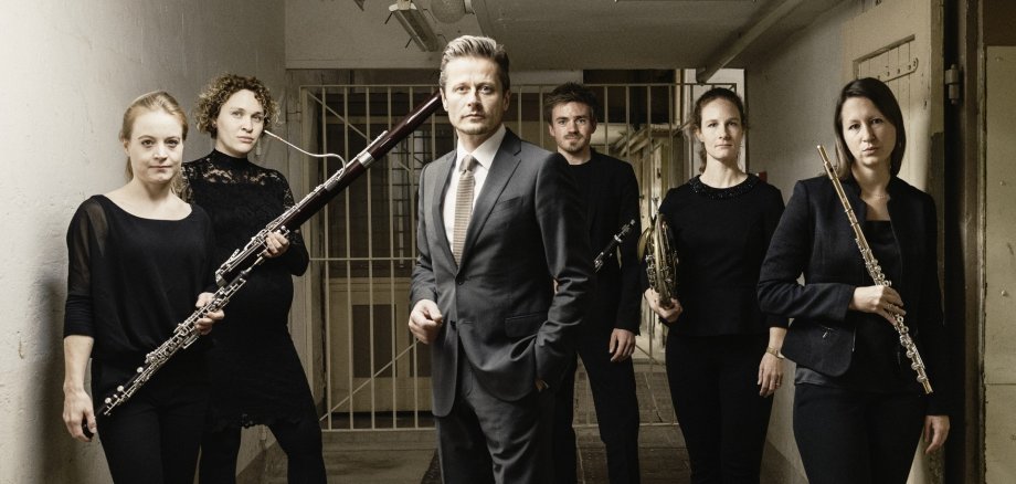 The photo shows Roman Knižka and the four female musicians and one male musician from Opus 45 standing in a corridor of the former Theresienstadt concentration camp. Roman Knižka stands in the foreground, the ensemble with instruments in a semi-circle behind him.