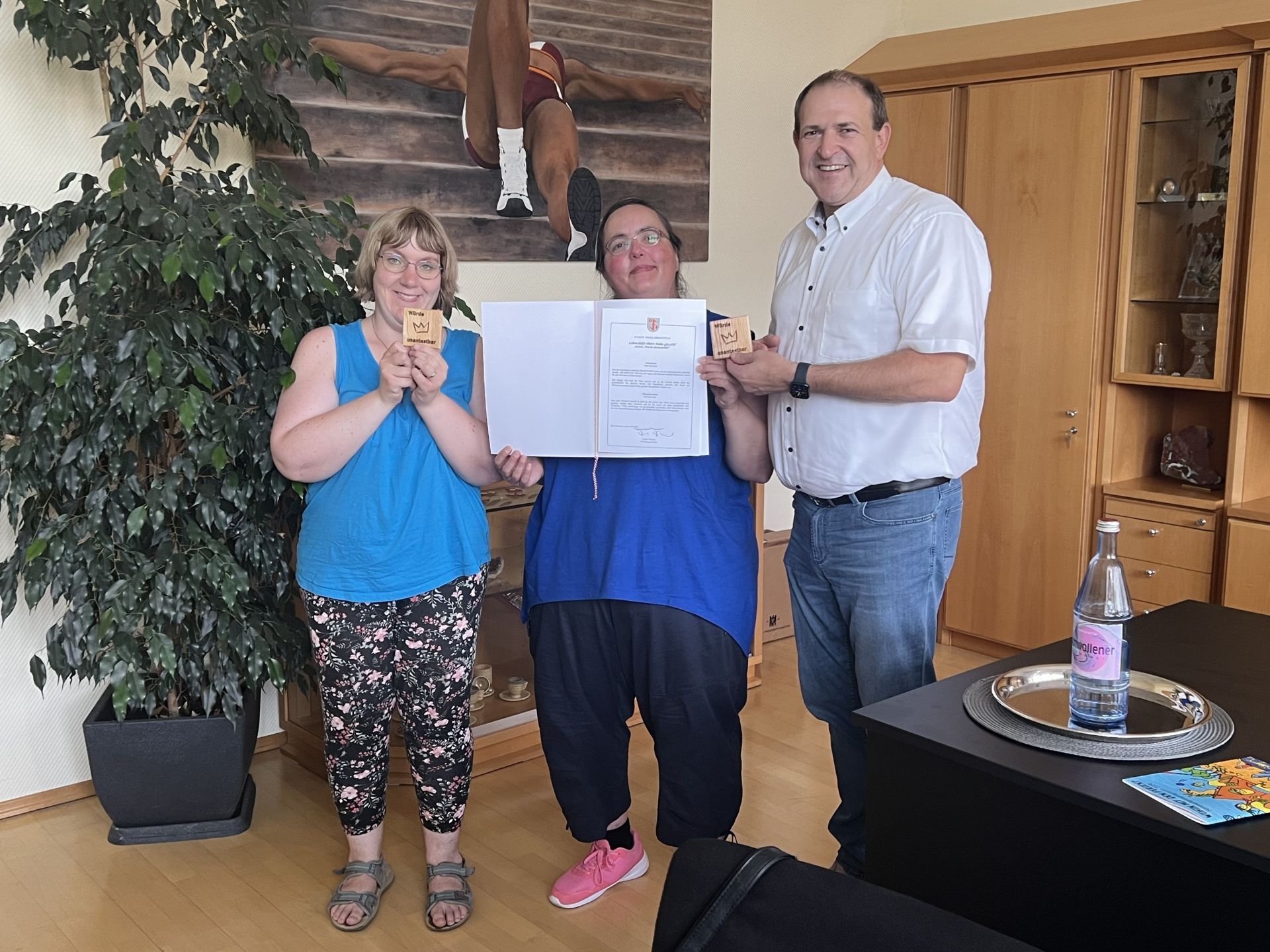 The photo shows Mayor Frühauf with two employees of the Nahe-Hunsrück workshops presenting him with "dignity plaques".