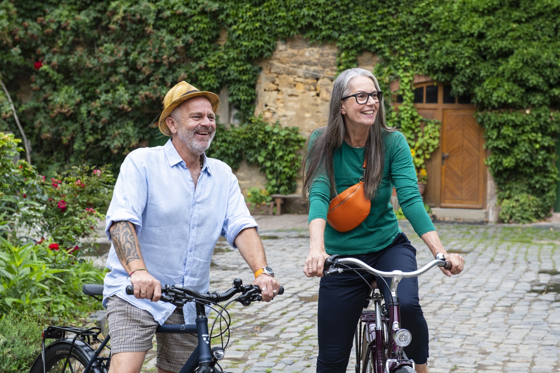 The photo shows a man and a woman. They are standing in a park with their bicycles and looking into the distance.