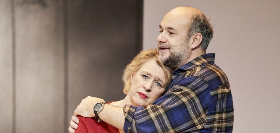 The photo shows a couple on stage. The woman is leaning on the chest of the man who is embracing her.
