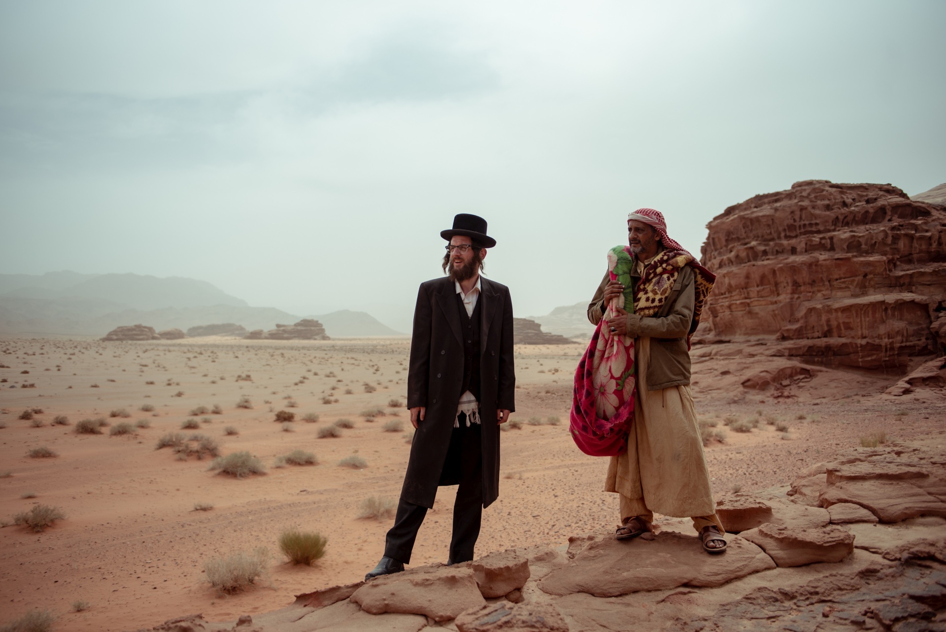 The photo shows two men standing in a desert. They are looking into the distance together.