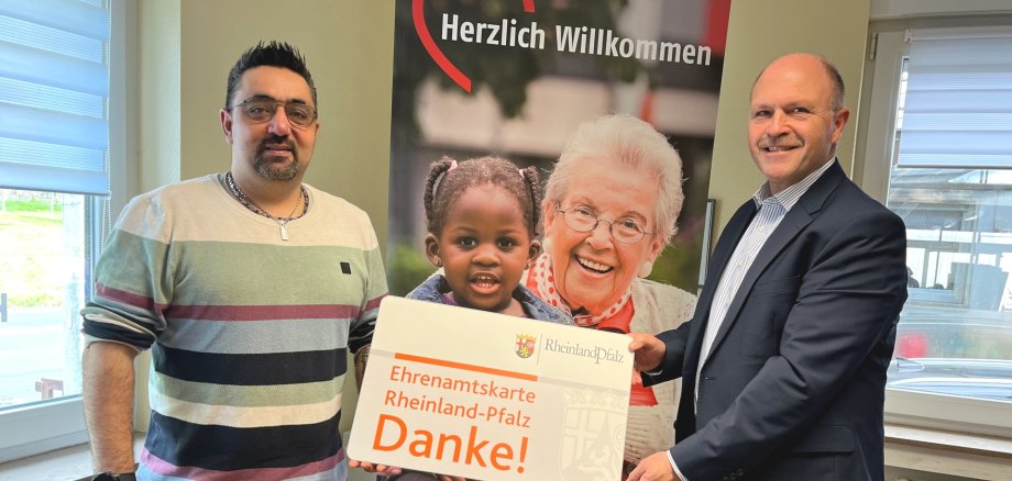 The photo shows the two people mentioned. They are holding an oversized volunteer card up to the camera together, with an AWO roll-up in the background.