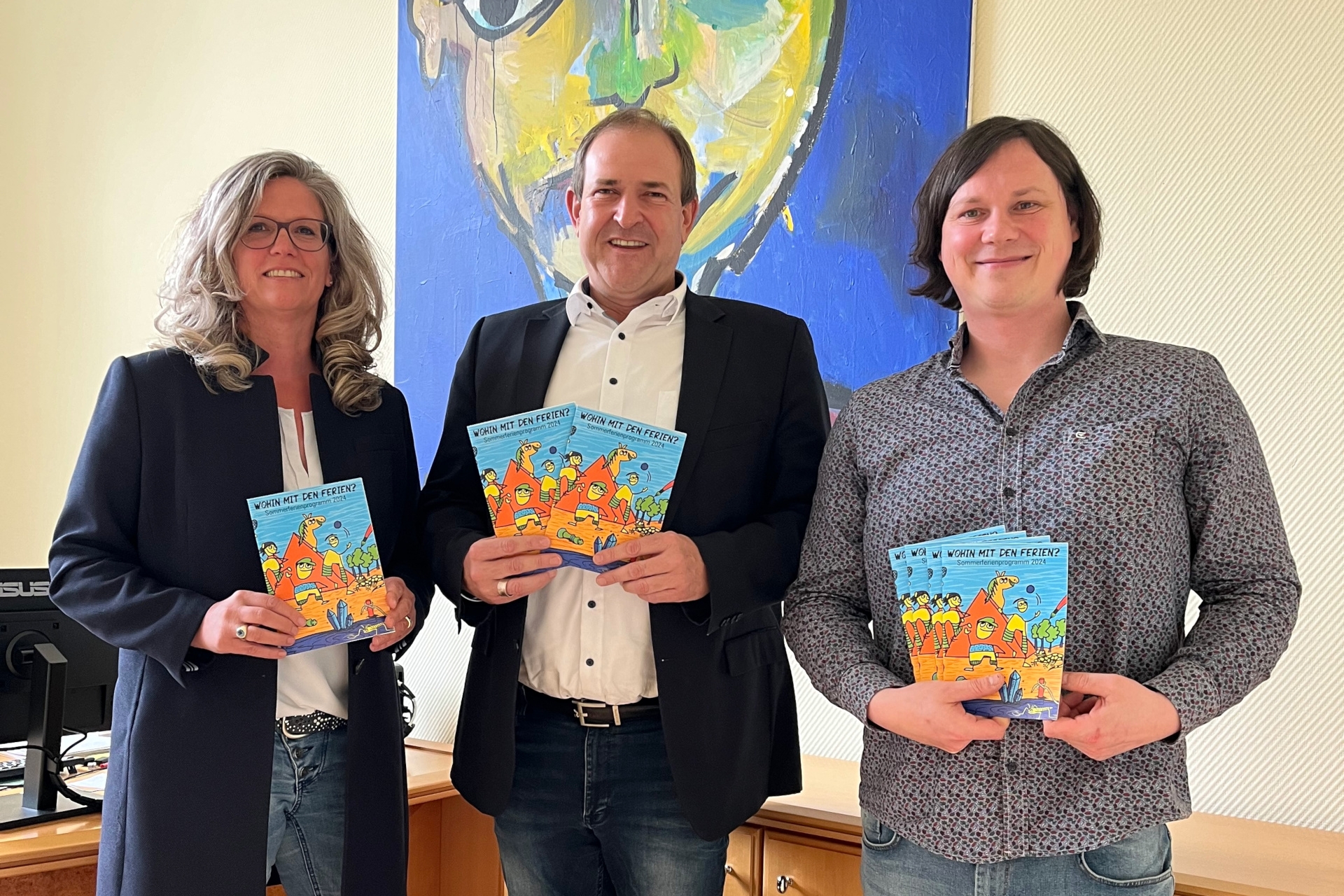 The photo shows the people mentioned. They are standing next to each other, holding vacation booklets and looking at the camera.