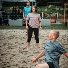 The photo shows three people on the beach volleyball court.