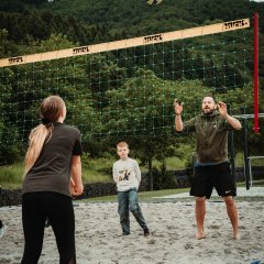 The photo shows people on the beach volleyball court.