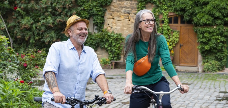 The photo shows a man and a woman. They are standing in a park with their bicycles and looking into the distance.