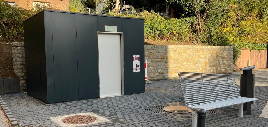 The photo shows the toilet block and the benches with garbage cans in front of it.