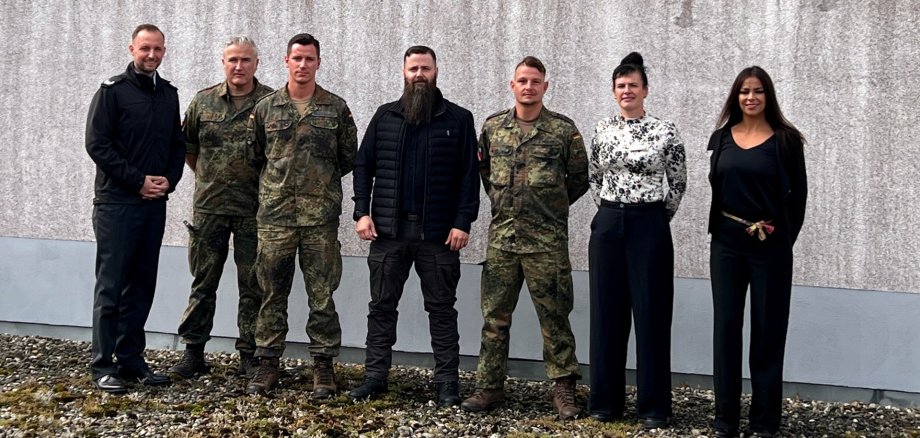 The photo shows the aforementioned people standing next to each other in front of a wall and looking into the camera.