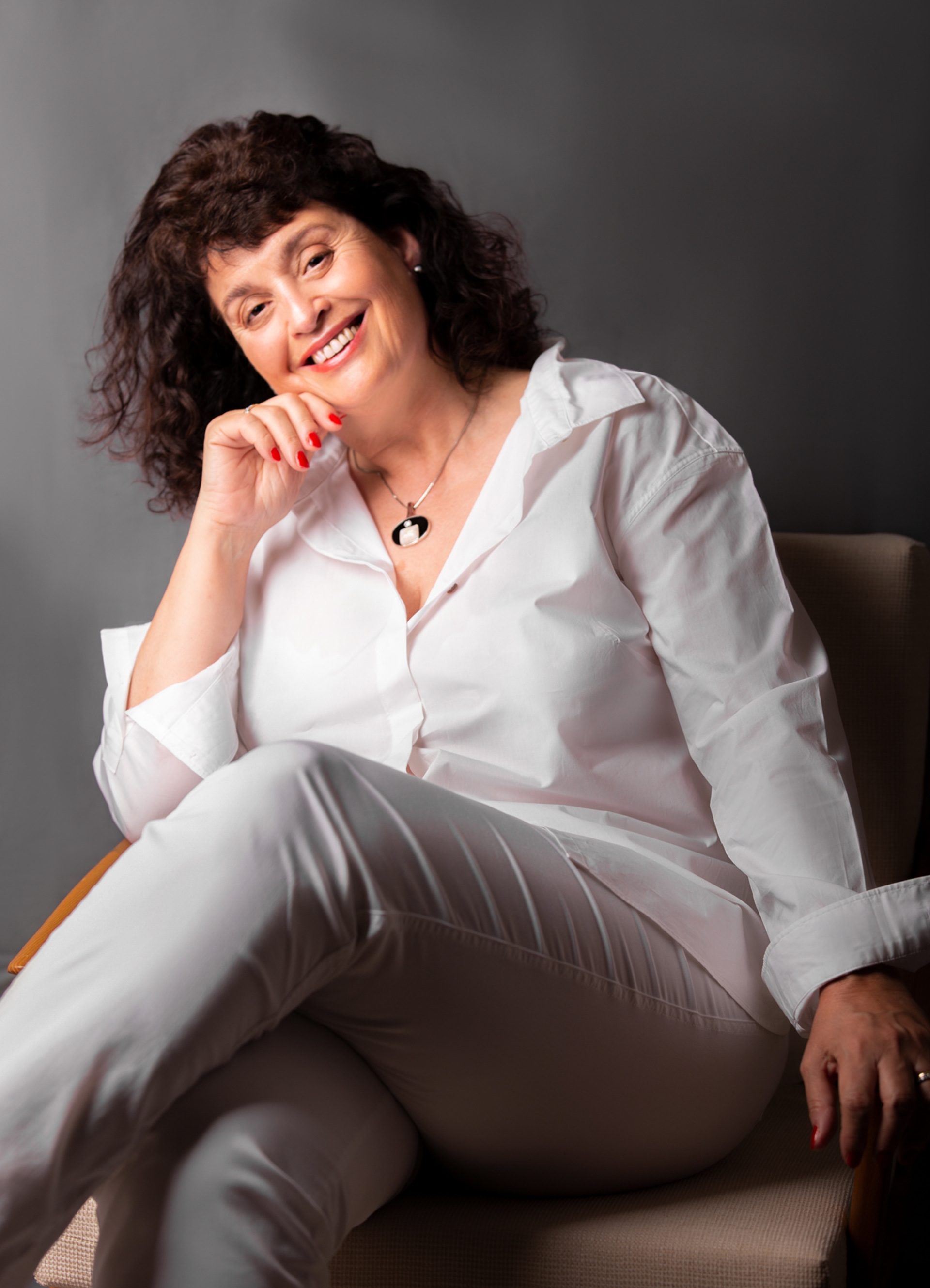 The photo shows Tessa Duncan. She is sitting in an armchair, resting her chin on one hand and smiling at the camera.