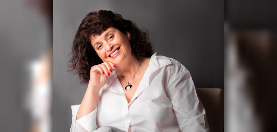 The photo shows Tessa Duncan. She is sitting in an armchair, resting her chin on one hand and smiling at the camera.