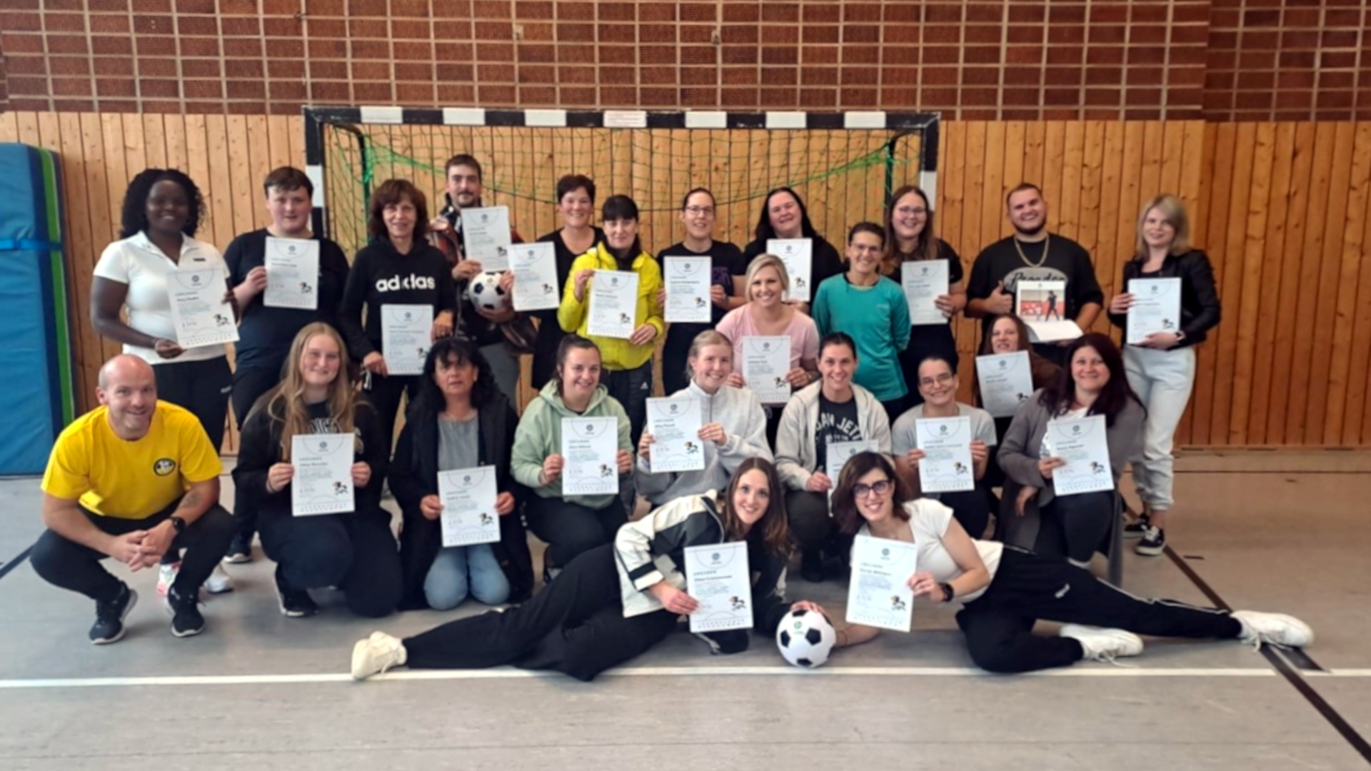 The photo shows the participants and the instructor of the training course. They are standing in three rows in a gym. The back row is standing, the middle row is kneeling and two more people are lying in front of them.