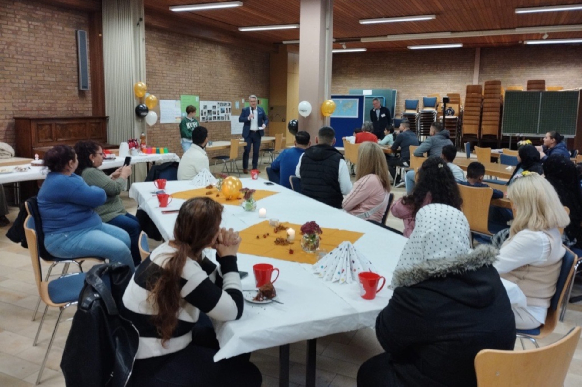 The photo shows many people sitting at tables. They are looking at District Administrator Kowalski, who is standing in the background of the picture and speaking into a microphone.