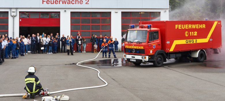The photo shows the courtyard of fire station 2. Three members of the youth fire department "extinguish" the "fire" of a fire engine. They are watched by numerous visitors to the event.