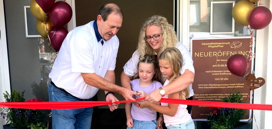 The photo shows Mayor Frühauf and Franziska Schhmit as well as two girls; the entrance area of the health center can be seen in the background. The four people are standing behind a red ribbon, the mayor has a pair of scissors in his hand and is about to cut the ribbon.