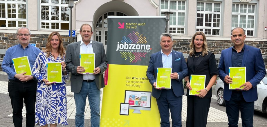 The photo shows the aforementioned people standing next to each other in front of the façade of the Stadthaus and looking into the camera. Each person is holding a "jobzzone" in their hand. In the middle is a roll-up display with the inscription "jobzzone".