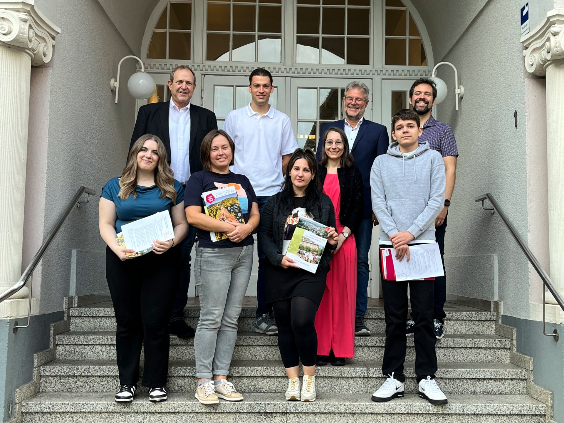 The photo shows the people mentioned in the article. They are standing on the steps in front of the town hall and looking into the camera.