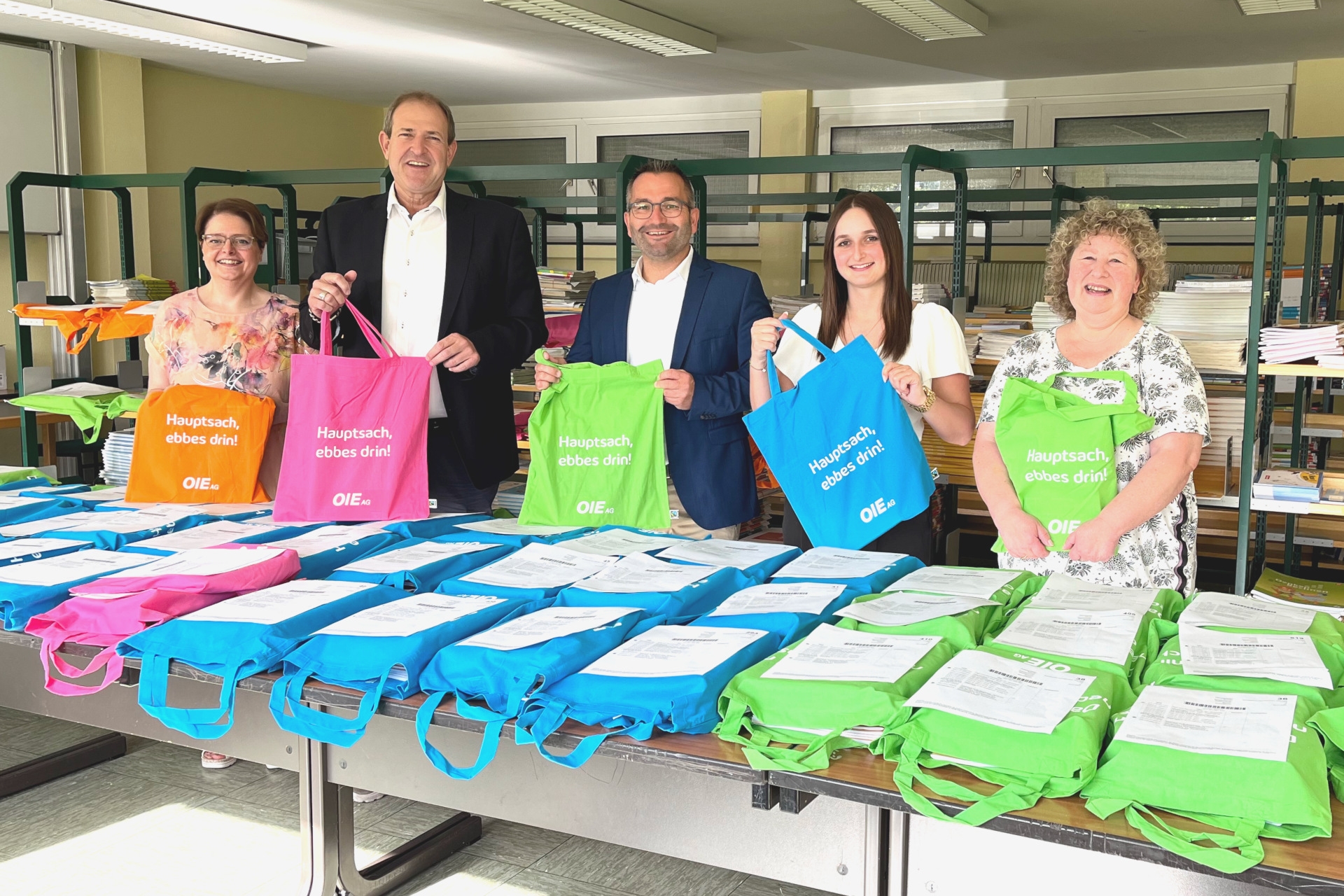 The photo shows the people mentioned. They are standing next to each other behind a table with stacks of filled bags. The people are each holding a bag and looking at the camera.